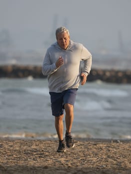 Long shot - vertical photo of an elderly man in a gray jacket and shorts leads an active lifestyle, running along the seaside