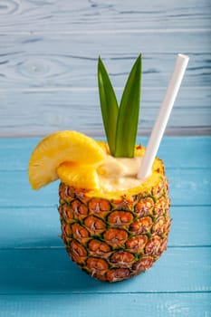 Vertical photo of exotic pineapple cocktail Pina colada on a blue wooden background