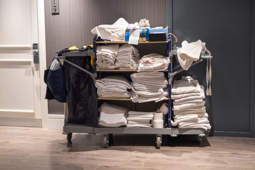 Horizontal photo of a trolley for a hotel maid, standing in front of a room, with clean towels and robes