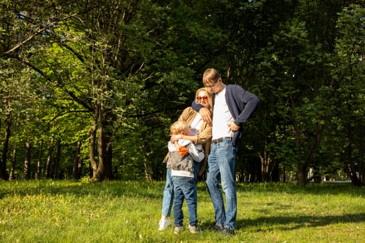 White Hugging Family. Mother, Father, Child Boy Stand In Park, Enjoying Time Together. Summer Time. Happy Parenthood, Family Leisure Time. Love And Care. Horizontal Plane. High quality photo