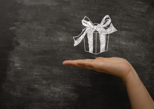 concept time to give gifts for the holidays. A woman's hand holds a drawn gift on a black board. Copy text.
