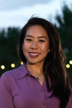 Vertical headshot of young smiling asian woman at sunset. Lifestyle.