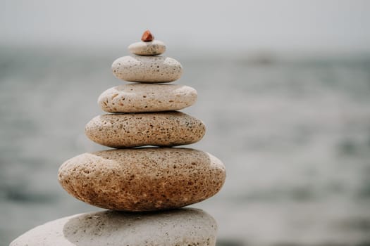 Pyramid stones on the seashore with warm sunset on the sea background. Happy holidays. Pebble beach, calm sea, travel destination. Concept of happy vacation on the sea, meditation, spa, calmness.