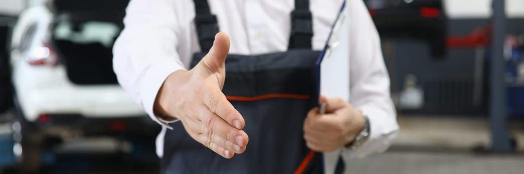 Closeup of auto mechanic greeting someone and offering handshake working in auto repair shop. Car service contract concept