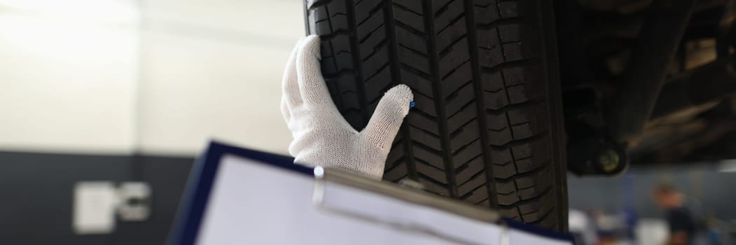 Auto mechanic technician holds blank clipboard sheet in hand with copy space text and car tires. Checking the quality of car tires concept