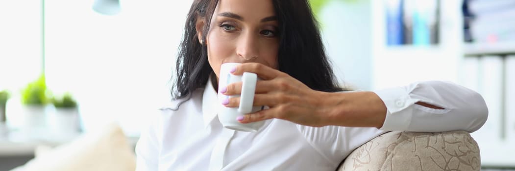 Thoughtful sad woman drinking from cup in office. Problems at work and depression concept