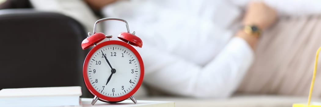 Alarm clock at seven o'clock and woman sleeping on couch. Fatigue and restful sleep concept