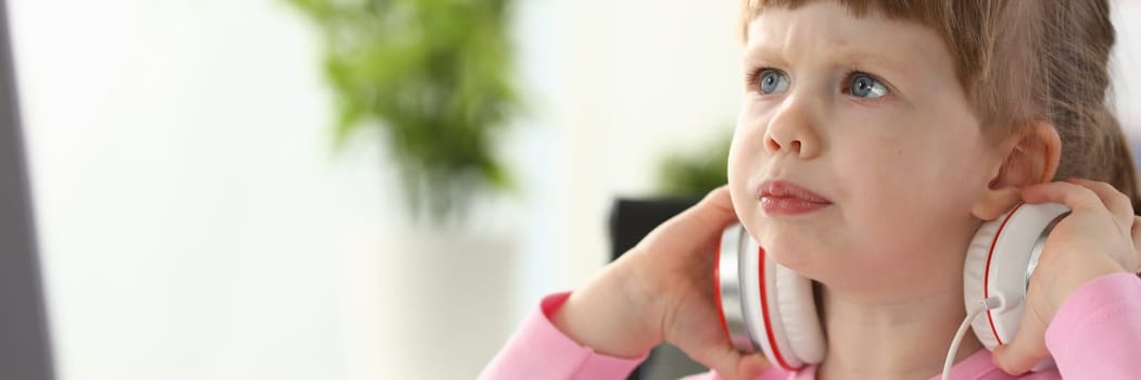 Portrait of a little beautiful child girl carefully looks at monitor in headphones. Interesting educational videos for kids concept