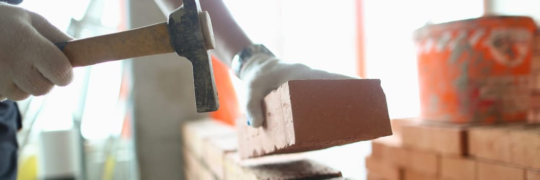 Industrial worker builds interior walls using hammer and level to place bricks into cement. Detail of worker with tools