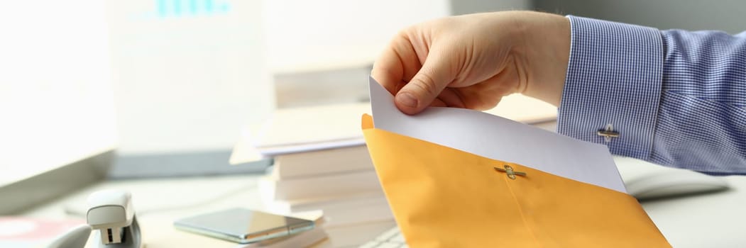 Businessperson opens yellow envelope with mail at workplace. Business correspondence and bank letter concept