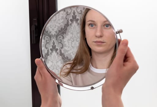 Portrait Of Caucasian Smiling Young Female After Eyelash Lamination Procedure Looking At Own Reflection In Mirror. Horizontal Plane High quality photo
