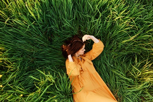 a close horizontal photo of a pleasant woman in a long orange dress resting lying in the tall grass straightening her hair. Street photography, the theme of privacy with nature. High quality photo