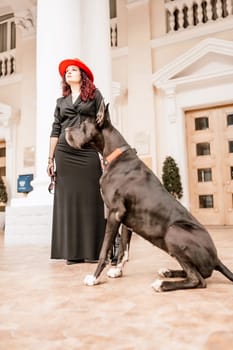 A photo of a woman and her Great Dane walking through a town, taking in the sights and sounds of the urban environment.