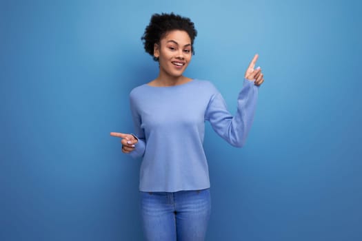 confident pretty brunette lady with afro curls showing super hand gesture on blue background with copy space.