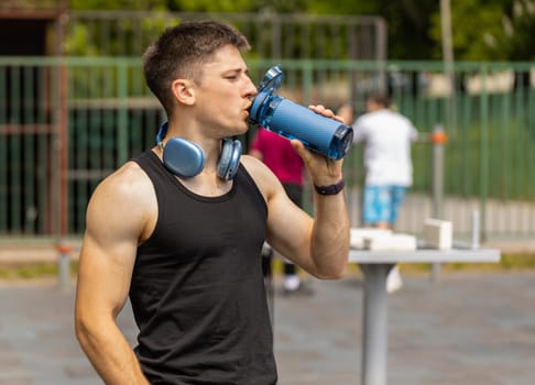Dehydrated thirsty athletic caucasian muscular man drinking water from bottle. Tired exhausted guy on playground. Sports, health, fitness routine, workout. Runner after difficult jogging outdoors
