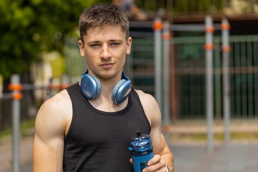 Portrait of athletic caucasian muscular man in sportswear holding drinking water bottle. Guy on playground before cardio workout exercises. Sports health fitness routine. Motivation. Outdoors gym