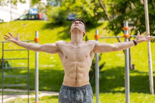 Athletic caucasian topless muscular man stretching body, warm up before cardio workout exercises. Young guy on playground. Sports, health, fitness routine workout. Strength and motivation. Outdoor gym