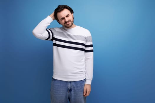 handsome well-groomed young brunette man thinking while standing on a blue background with copy space.