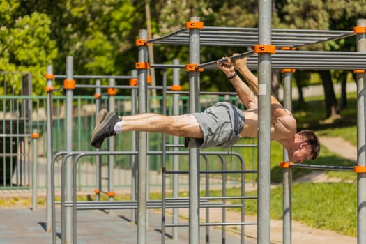 Athletic topless muscular man doing gymnastics exercise, strength elements, physical freestyle fitness workout. Young shirtless guy on playground. Sports health routine. Motivation. Outdoors gym