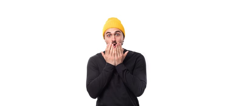 surprised handsome young 30 year old guy dressed in a black jacket and a yellow hat on a white background with copy space.