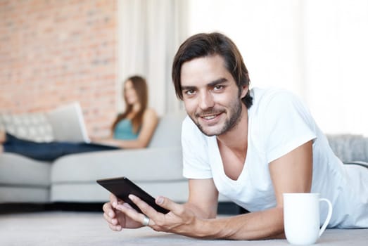 Technology makes me happy. Attractive young man lounging at home using his tablet