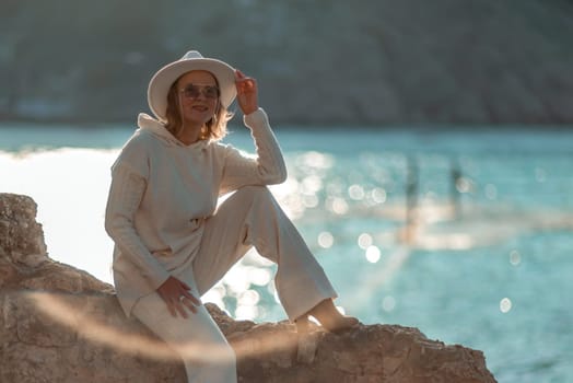 Happy blonde woman in a white suit and hat posing at the camera against the backdrop of the sea.