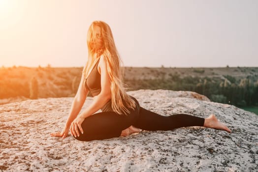 Well looking middle aged woman with long hair, fitness instructor in leggings and tops doing stretching and pilates on the rock near forest. Female fitness yoga routine concept. Healthy lifestyle.