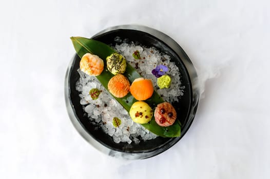 Temari sushi on a black plate with ice and bamboo leaf