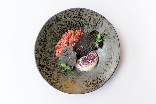 Exquisite serving of beef tartare on a black plate on a white background