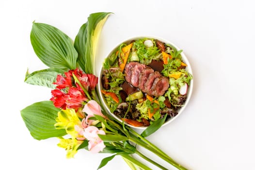 Salad with medium roasted beef and greens on a white plate decorated with bright flowers on a white background