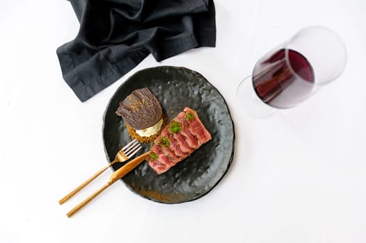 Exquisite serving of medium roasted beef slices on a black plate on a white background