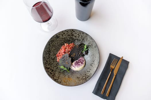 Exquisite serving of beef tartare on a black plate on a white background