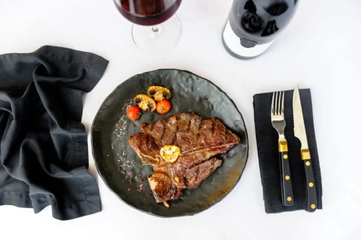 Exquisite serving of bone-in beef steak on a black plate on a white background