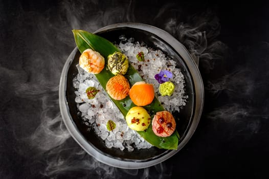 Temari sushi on a black plate with ice and bamboo leaf