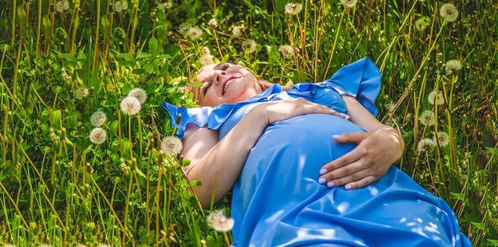 Pregnant woman with dandelions in the garden. Selective focus. Nature.