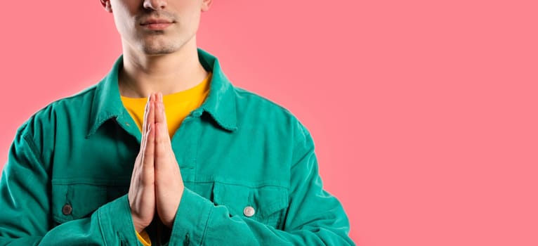 Young man praying with crossed fingers on pink background. Guy begs someone satisfy desires, help with, prays for luck in exam. Copy space. High quality
