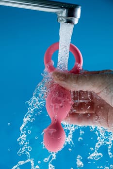 Woman holding pink anal beads under running water on blue background. Sex toy hygiene concept