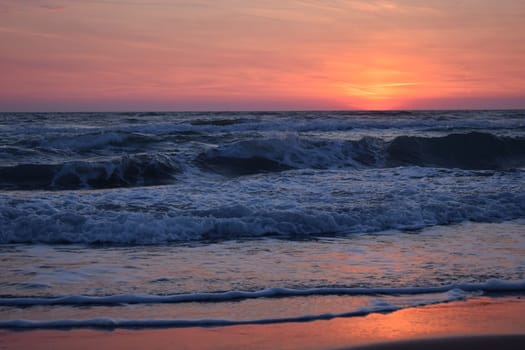 A beautiful sunset on the beach in the turbulent ocean. Shades of orange and blue.