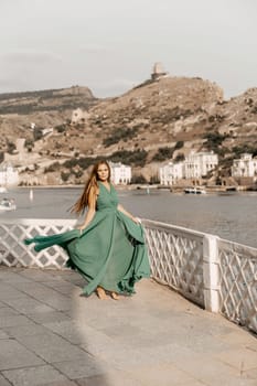 Woman sea trevel green dress. Side view a happy woman with long hair in a long mint dress posing on a beach with calm sea bokeh lights on sunny day. Girl on the nature on blue sky background