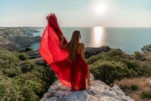 Woman sunset sea red dress, back view a happy beautiful sensual woman in a red long dress posing on a rock high above the sea on sunset