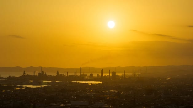 Low sun in orange sky over factory smokestacks by industrial city. High quality photo