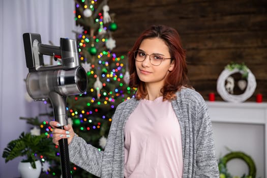 A young pretty girl is standing and holding a vacuum cleaner. At any time it is necessary to take care of tidiness and especially before any important holiday.