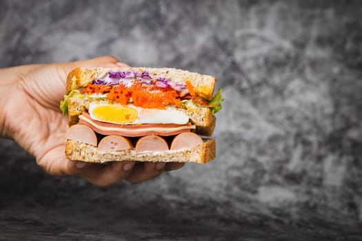 Hand holding a delicious sandwich on dark background for bakery, food and eating concept