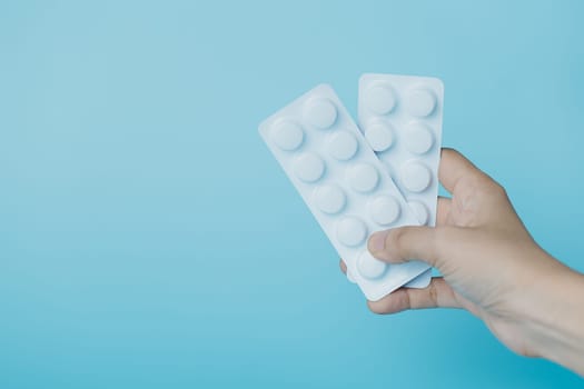 Hand holding a blister pack of medicine pill on blue background for medical and healthcare concept