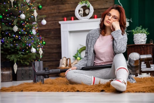 The girl sits on the floor and on her knees and three vacuum cleaner. A short rest after an intensive vacuuming of the entire house.