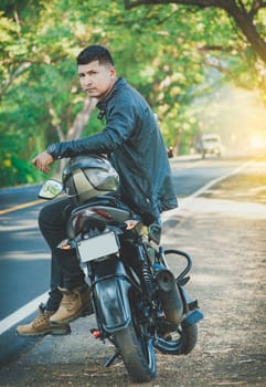 Portrait of biker in jacket sitting on his motorcycle at the side of the road. Latin motorcyclist sitting on his motorbike near a road