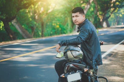 Latin motorcyclist sitting on his motorbike near an asphalt road. Portrait of biker in jacket sitting on his motorcycle at the side of the road