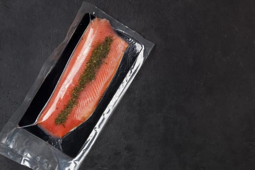 Fish fillet in vacuum packaging, on a black background. Red fish, trout.Copy space