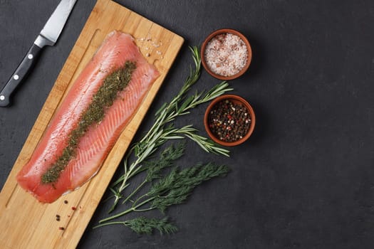 Salted fish fillet with spices and herbs:dill and rosemary on a wooden board on a black background. copy space