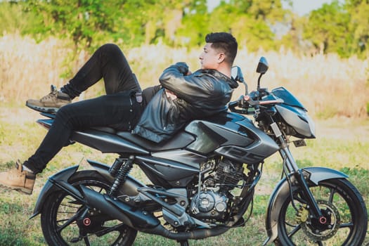 Biker man lying down on his motorbike outdoors. Motorcyclist in jacket lying on his motorcycle in the countryside